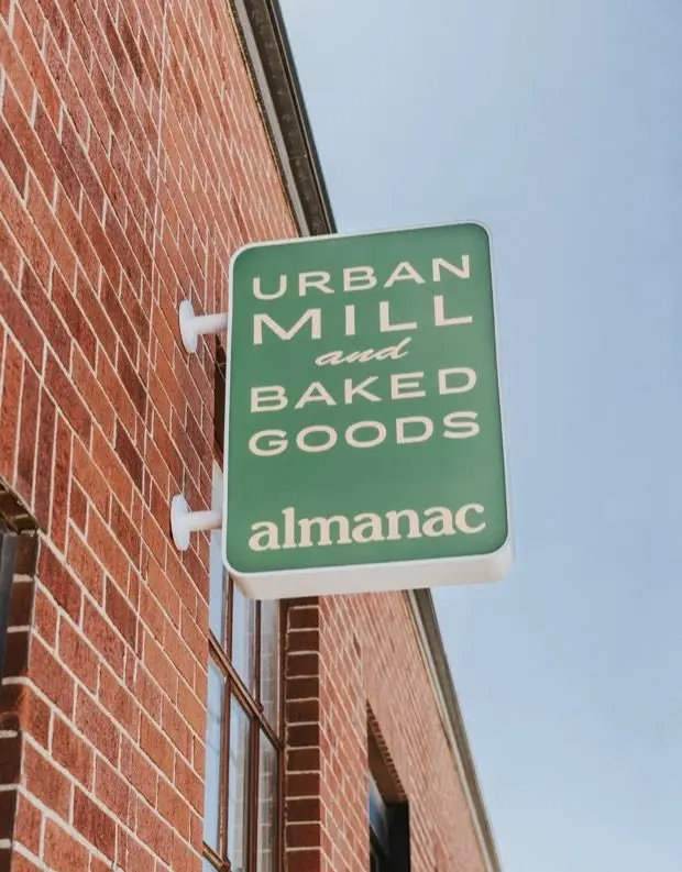 The green Almanac sign on the brick wall outside Little Italy, reading Urban Mill and Baked Goods.