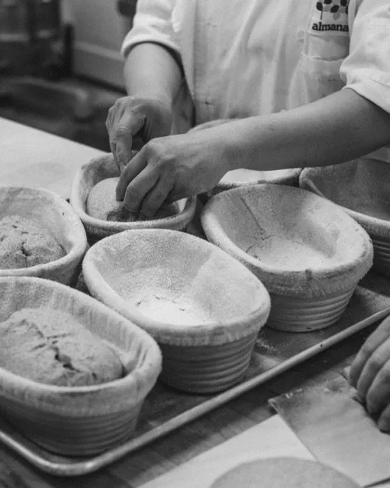 A baker setting shaped loaves into floured cane bannetons.
