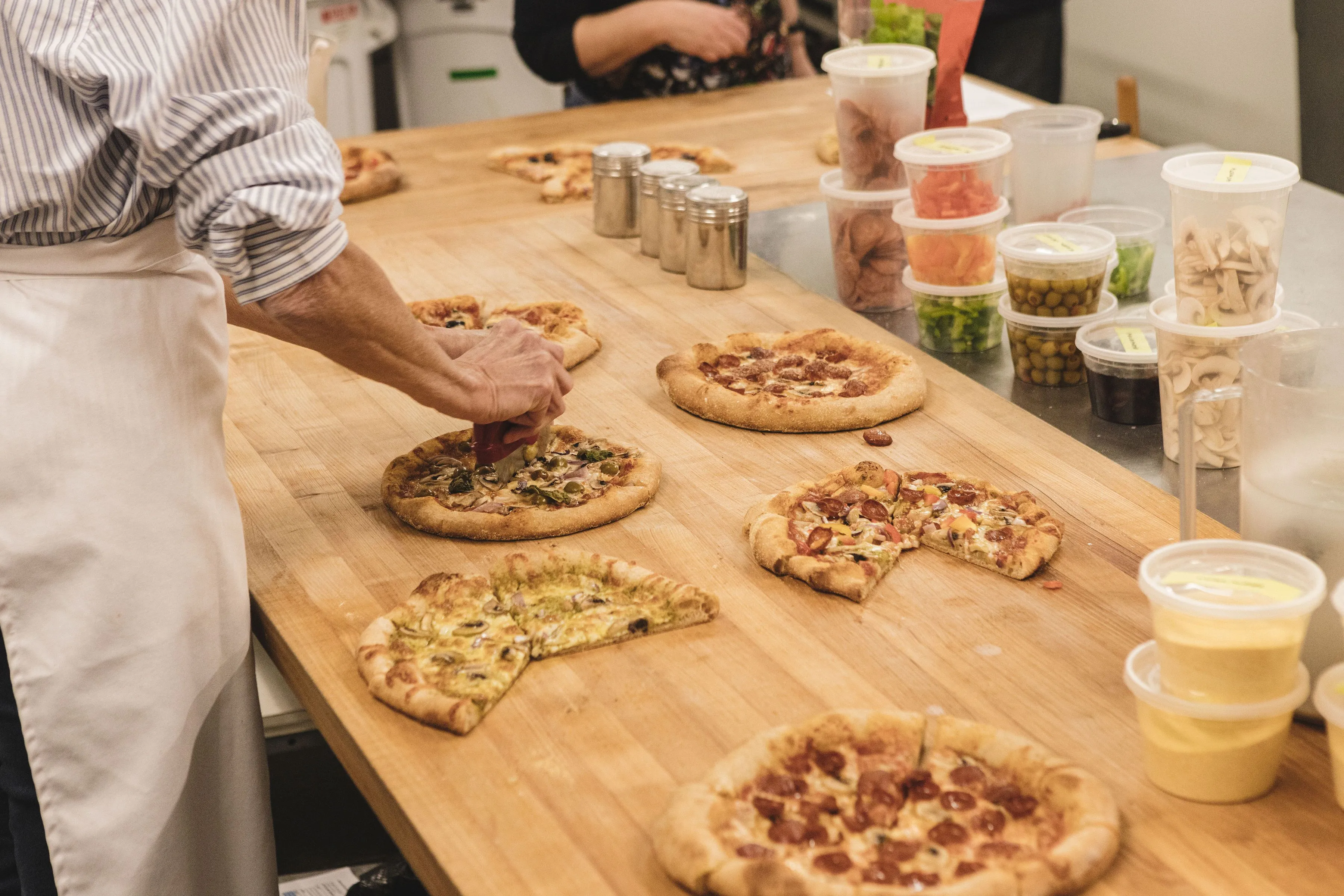 A long kitchen table with different types of pizza that workshop participants have made