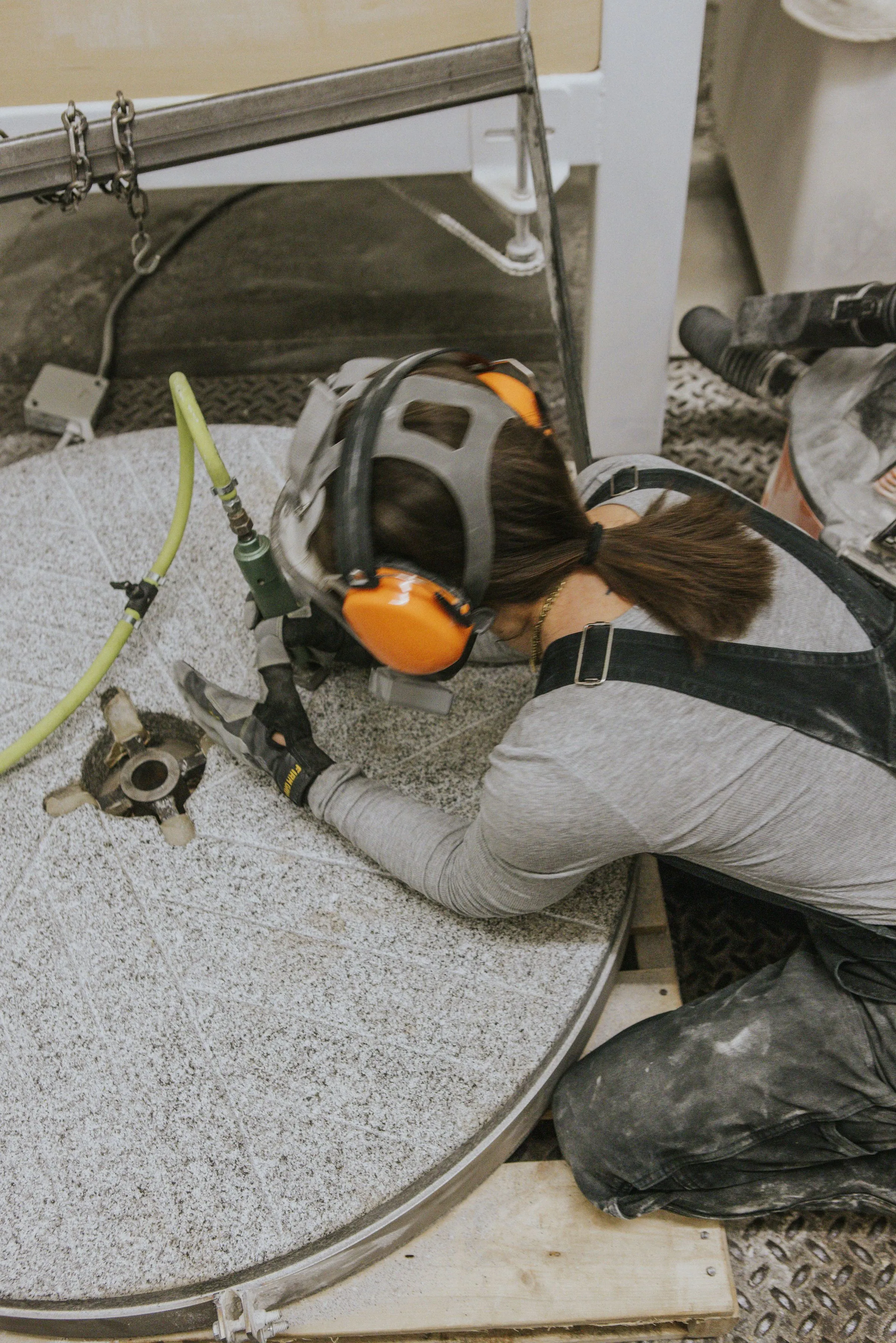 A woman bent over a mill stone with ear covers and a tool to sharpen the stone